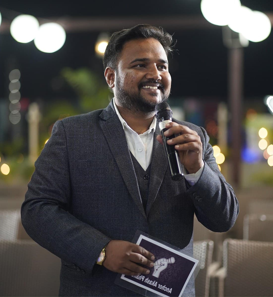 Anchor Akash Phalle holding a microphone at an evening event